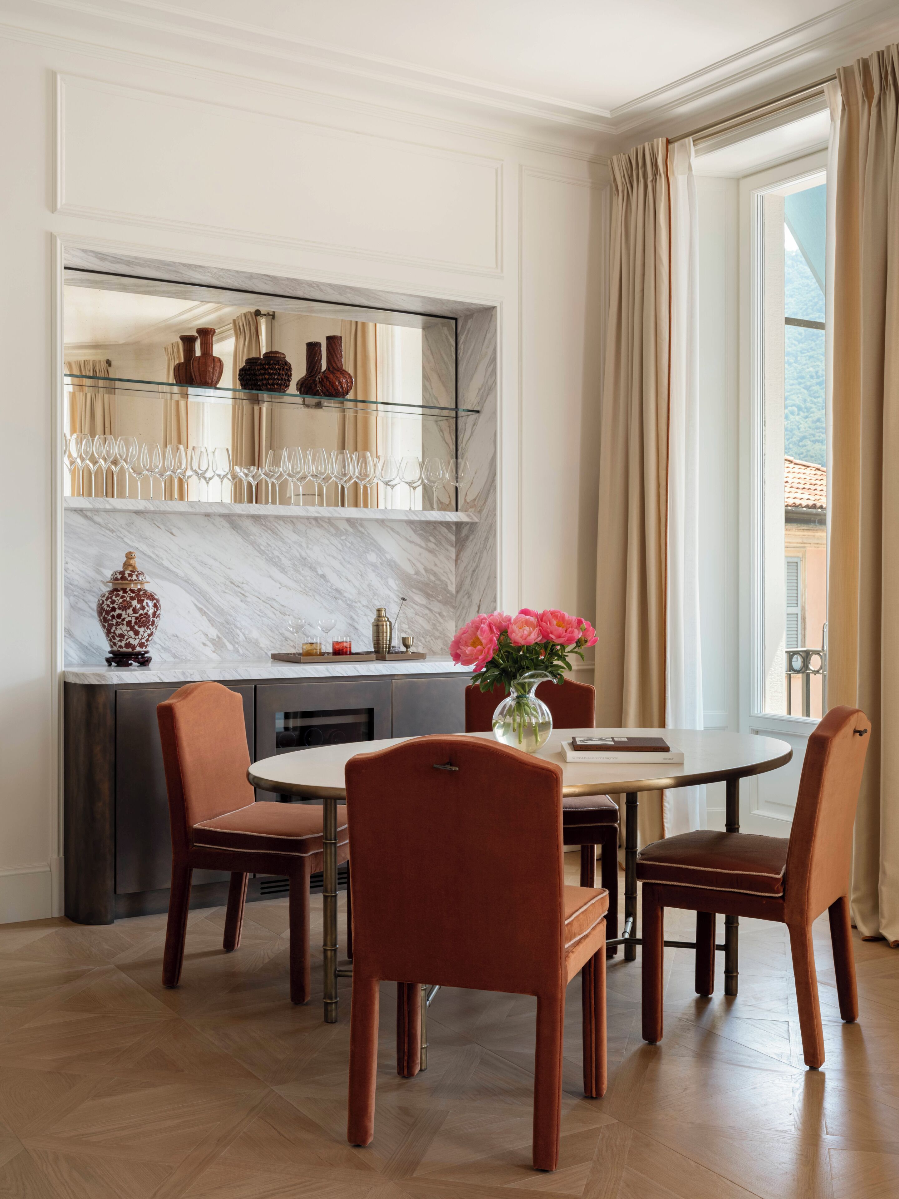 A dining area with a marble countertop, a glass shelf with wine glasses, and a vase with flowers.