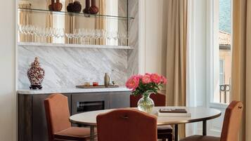 A dining area with a marble countertop, a glass shelf with wine glasses, and a vase with flowers.