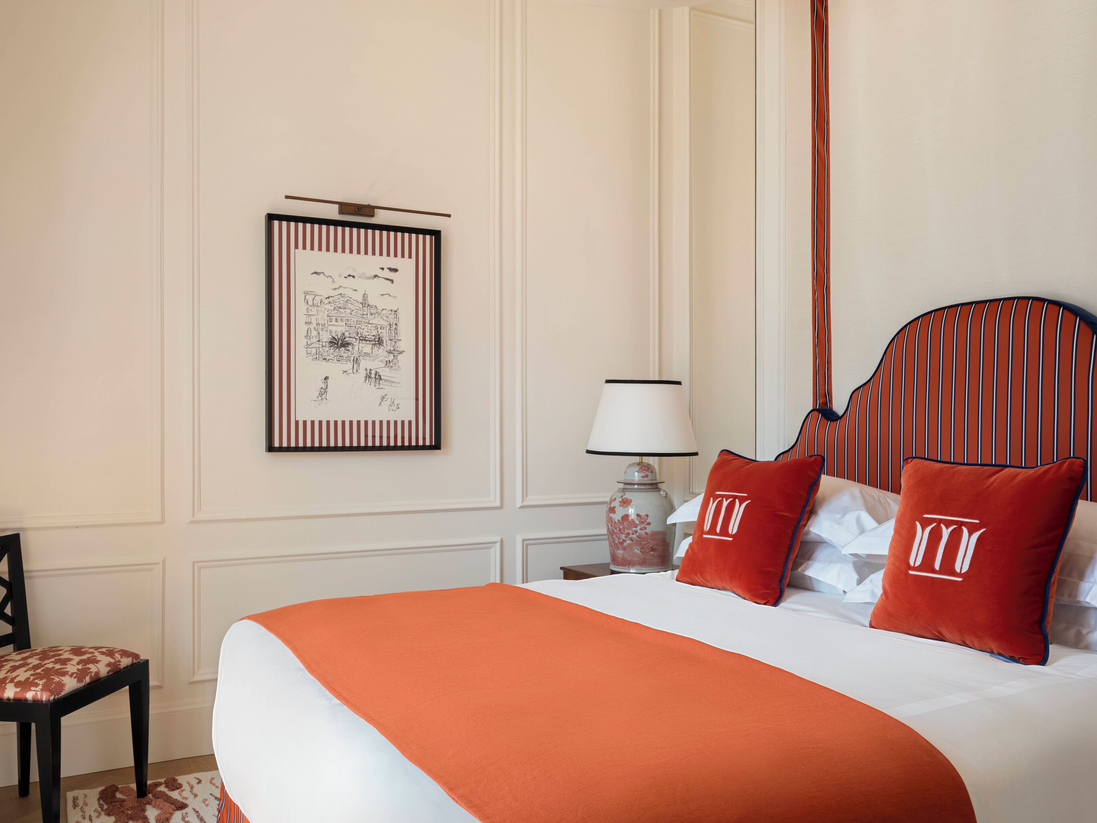 Habitación de hotel con una cama grande, una obra de arte enmarcada en la pared, una mesita de noche con lámpara y una silla.