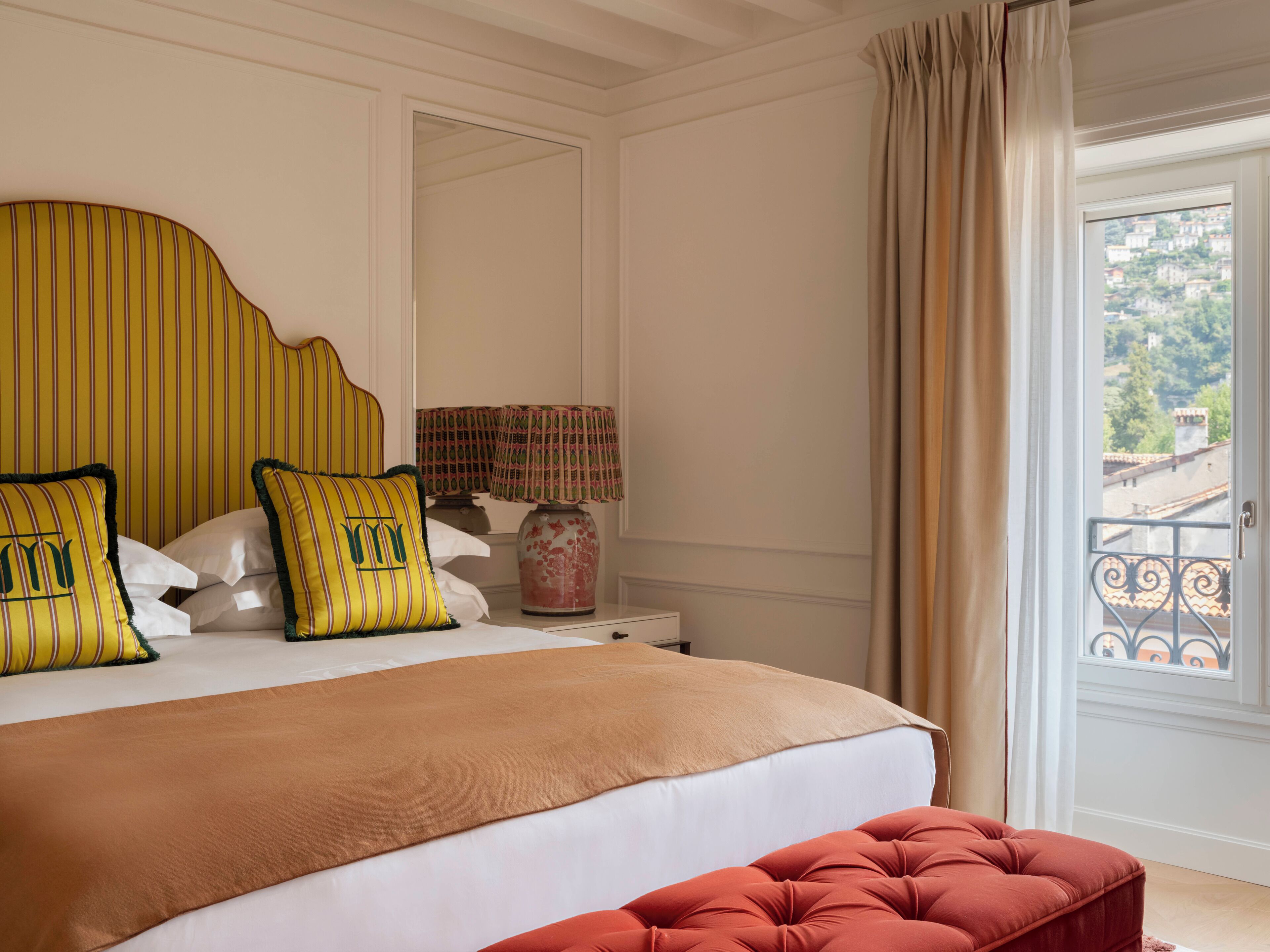 Een slaapkamer met een bed, nachtkastje, lamp en uitzicht.