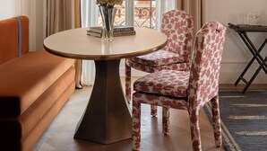 A room with a round table, two patterned chairs, a sofa, a small table with glasses, and a view of a building through a window with curtains. - Miralago Luxury Apartments (Cernobbio)