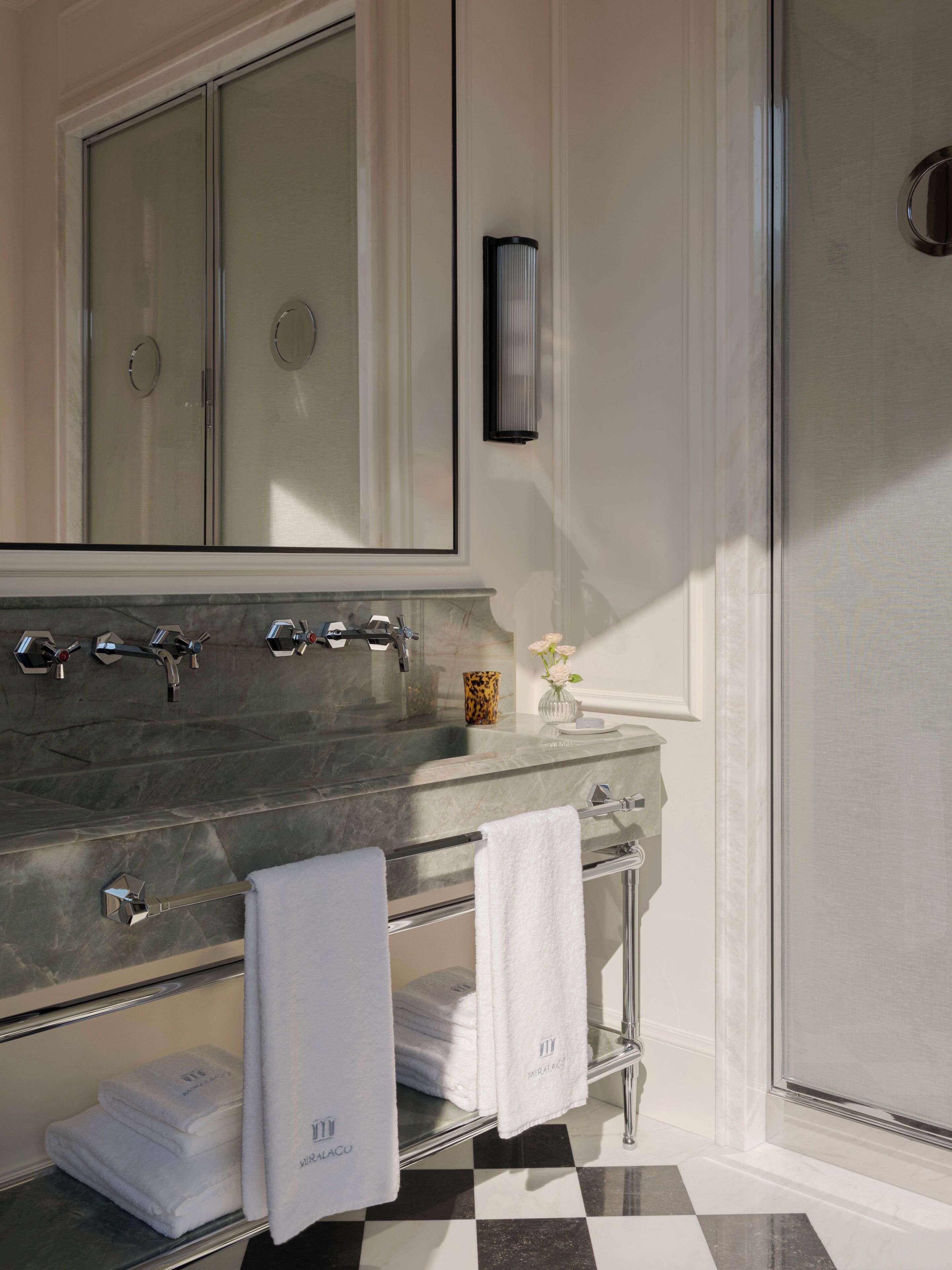 A bathroom with a large mirror, a marble sink, and a glass shower enclosure.