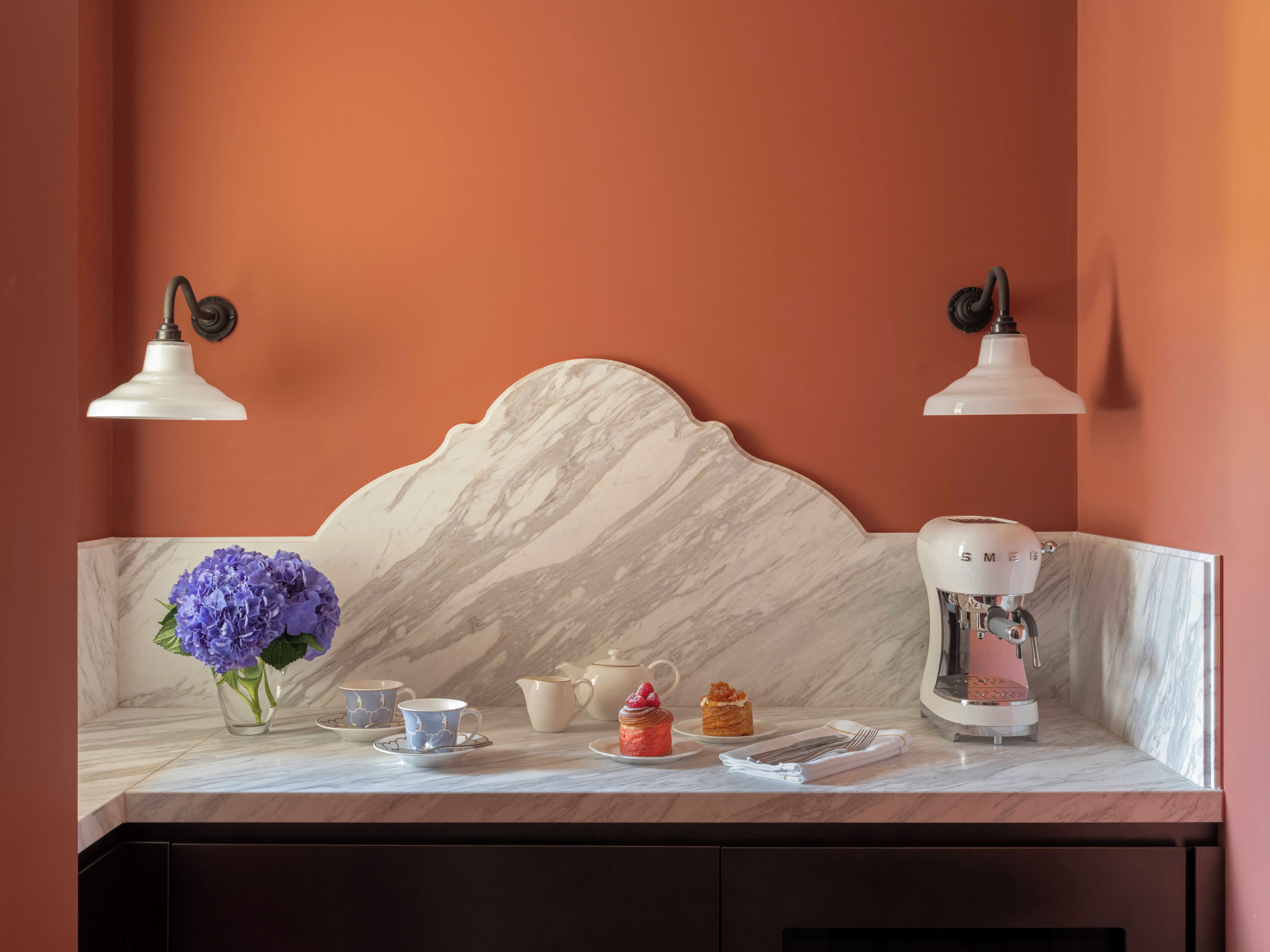 A kitchen counter with a marble backsplash, a coffee machine, and a vase of purple flowers.