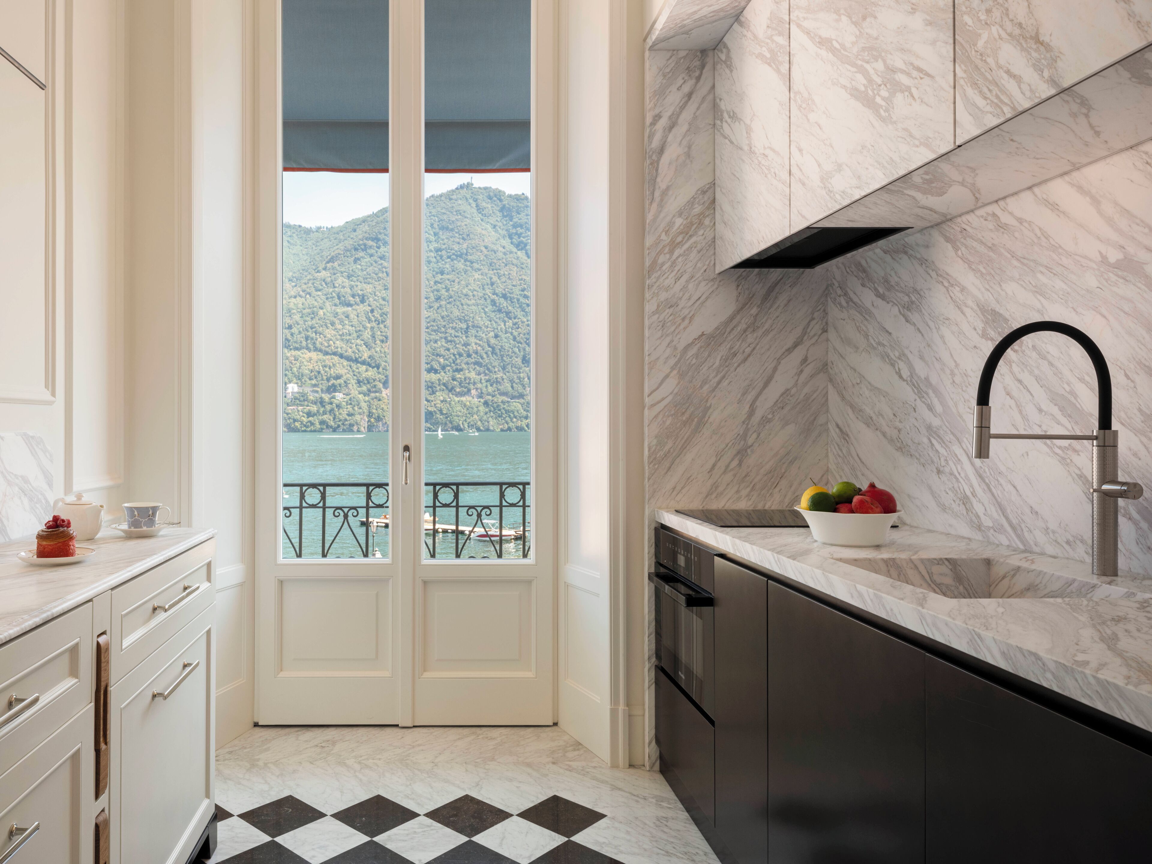A kitchen with a view of a lake and mountains, a black and white checkered floor, and a modern faucet.