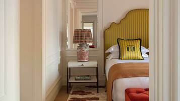 Una habitación de hotel con una cama, una mesita de noche, una lámpara, un banco rojo y una alfombra estampada.