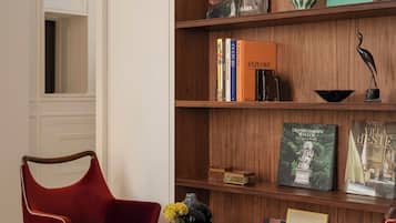 A room with a wooden bookshelf, a red chair, a small round table with a vase, and a book titled 'Grand Garden Italian'.