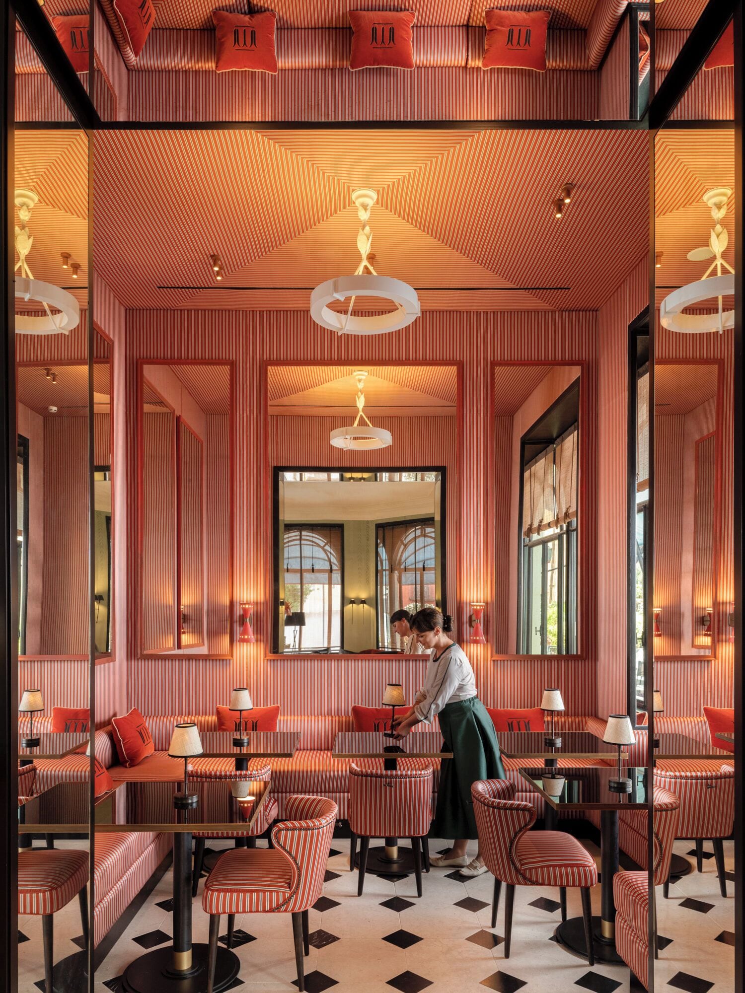 Interior de restaurante con paredes a rayas, asientos acolchados rojos y un espejo central.