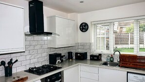 Una cocina moderna con armarios blancos, extractor de aire negro, horno empotrado, cafetera y ventana con persianas.