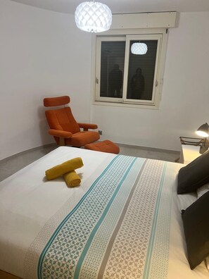 A bedroom with a bed, an orange chair, a window, and a lamp. - Les Appartements De Lina - L'Architek (La Grande-Motte)