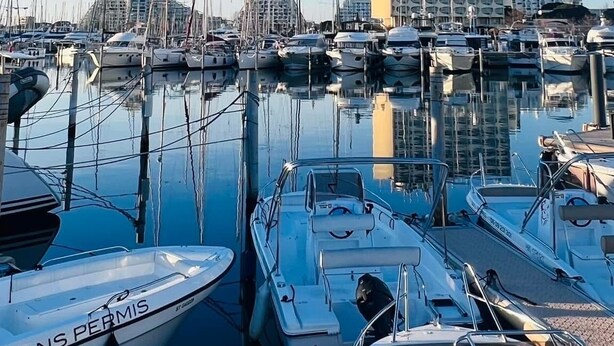 A marina with multiple boats docked, a building with a unique circular window design, and a clear blue sky. - Les Appartements De Lina - L'Architek (La Grande-Motte)