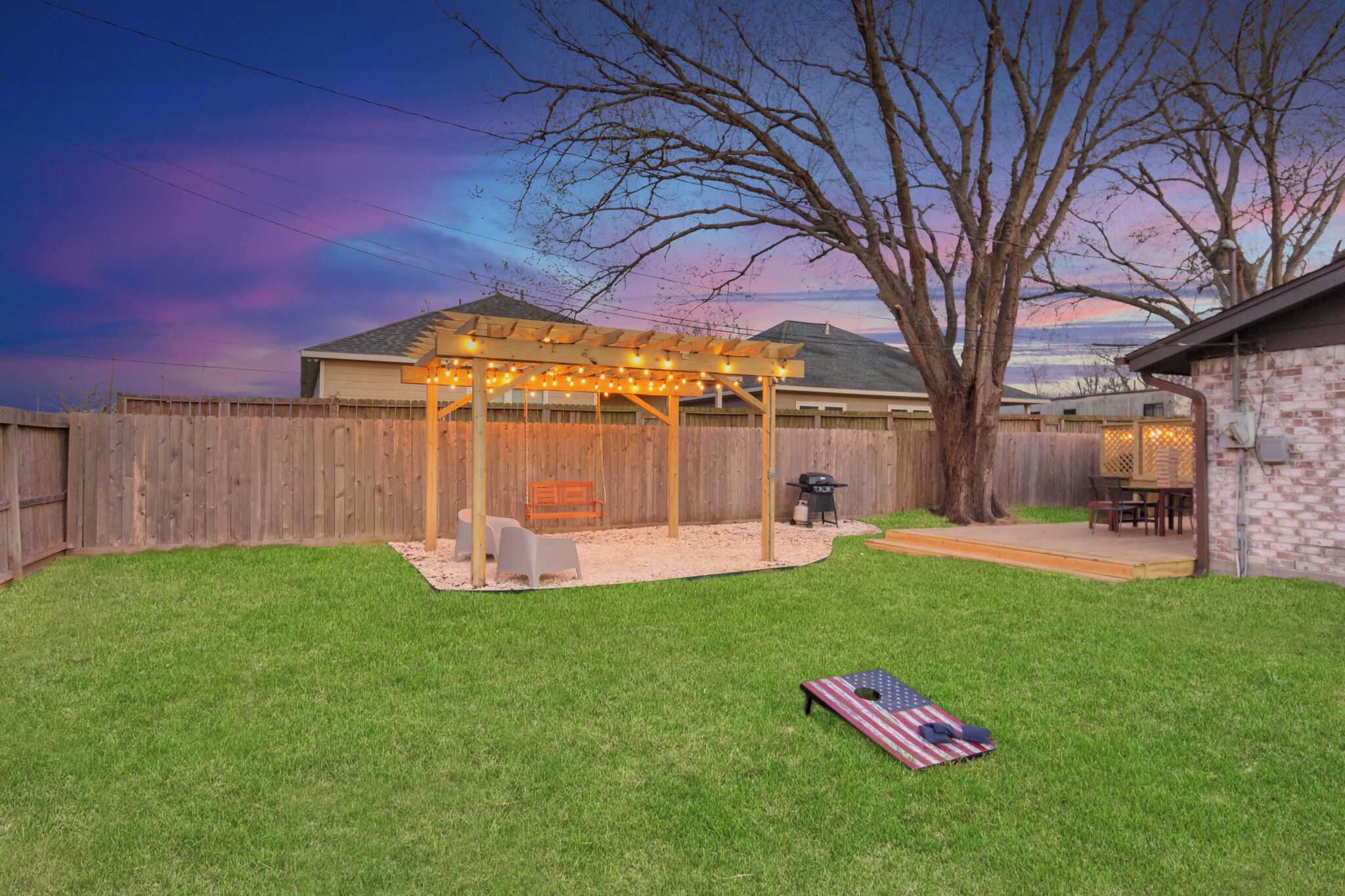 Un jardin avec une pergola en bois, un espace barbecue et une pelouse.