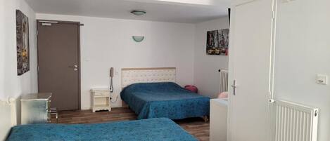 Une chambre avec deux lits, une table de chevet, une commode, un radiateur et une porte.
