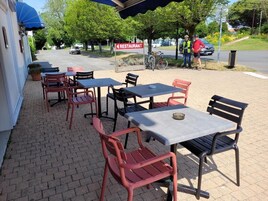 Un área de estar al aire libre con mesas y sillas, un letrero que indica un restaurante, y una bicicleta estacionada cerca.
