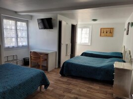 Una habitación con dos camas, un escritorio, una silla y una televisión en la pared.