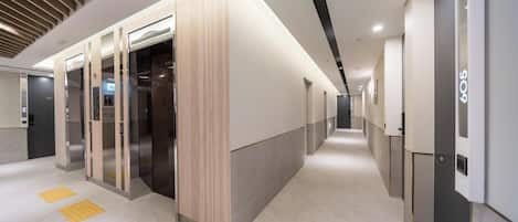 Un pasillo de hotel moderno con ascensores, una zona de recepción y un ambiente limpio y bien iluminado.