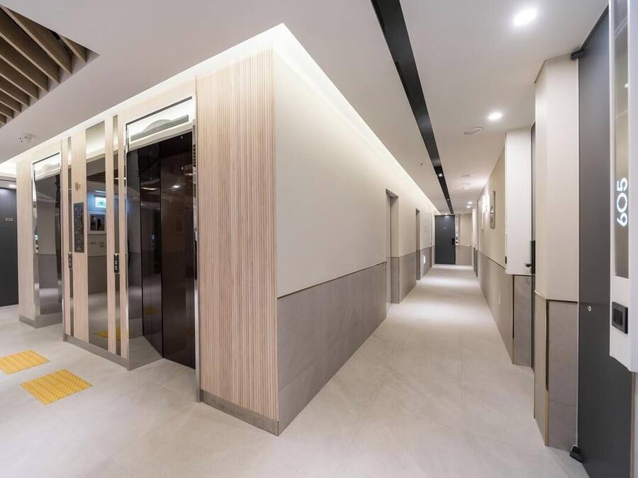 A modern hotel corridor with elevators, a reception area, and a clean, well-lit environment.