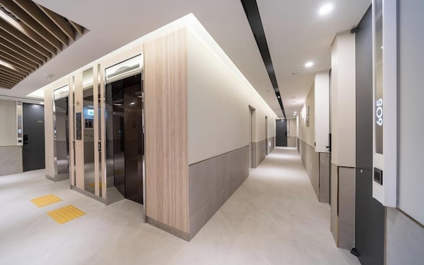 A modern hotel corridor with elevators, a reception area, and a clean, well-lit environment.