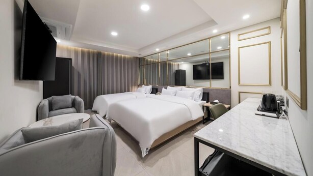 A modern hotel room with a large bed, two bedside tables, a flat-screen TV, a seating area with a sofa and armchair, and a marble-topped desk. - Incheon Hound New Town Branch (Incheon)