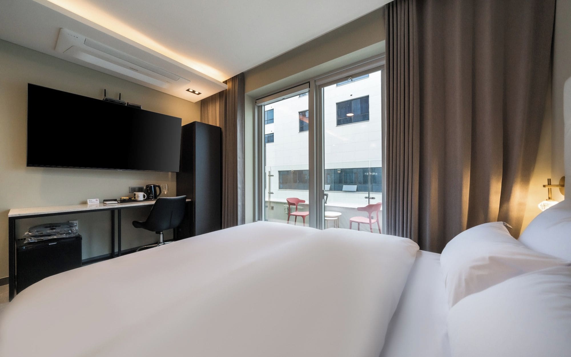 A hotel room with a bed, a desk with a chair, a television, and a window with curtains.