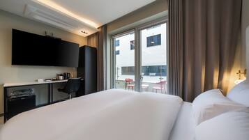 A hotel room with a bed, a desk with a chair, a television, and a window with curtains.