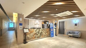 A hotel reception area with a stone wall, a reception desk, a sofa, and a vending machine. - Incheon Hound New Town Branch (Incheon)