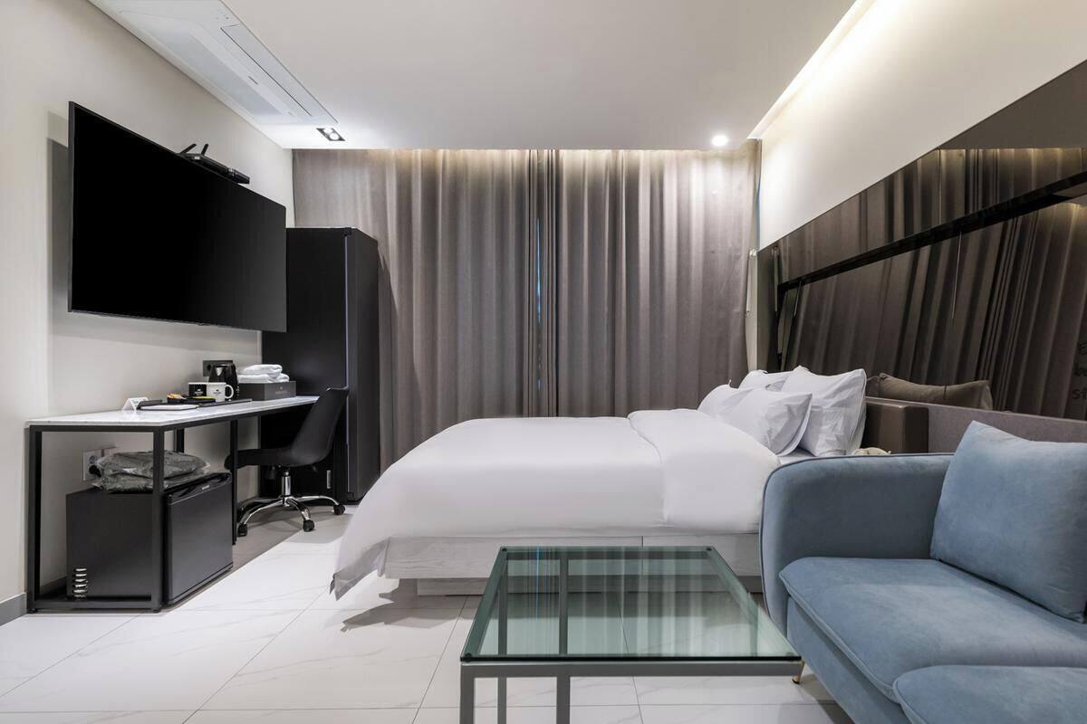 A modern hotel room with a bed, a sofa, a desk, a television, and a curtain.