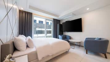 A modern hotel room with a large bed, a TV, a seating area, and a balcony with a view.