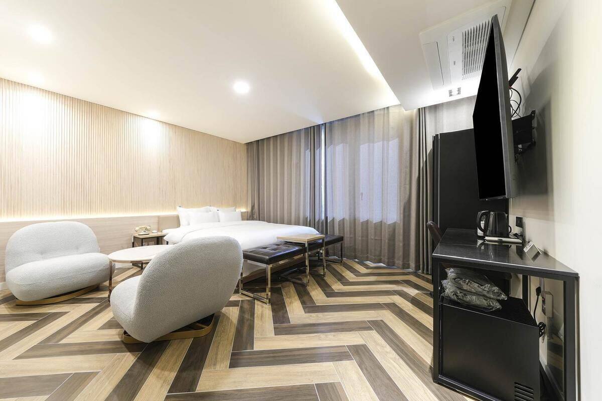 A modern hotel room with a bed, two armchairs, a small table, and a TV.