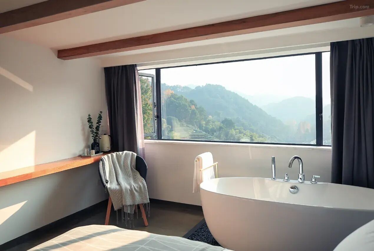 A modern bathroom with a large bathtub, a window with a mountain view, a wooden bench, and a towel rack.