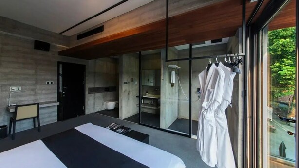 Habitación de hotel moderna con una cama grande, zona de estar, baño y vistas al exterior.