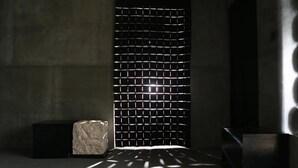 Una habitación con pared de diseño geométrico, una escultura de piedra y un mueble negro moderno.