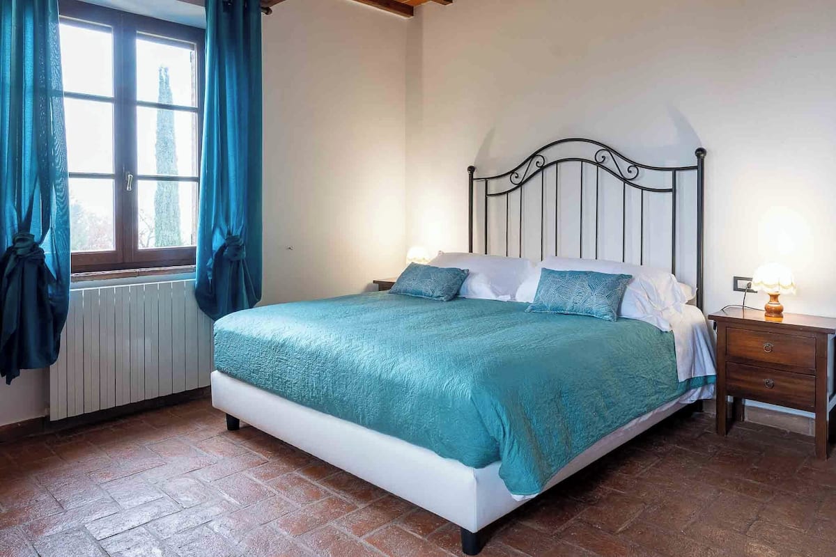 Een slaapkamer met een bed, nachtkastje, raam met gordijnen en een radiator.