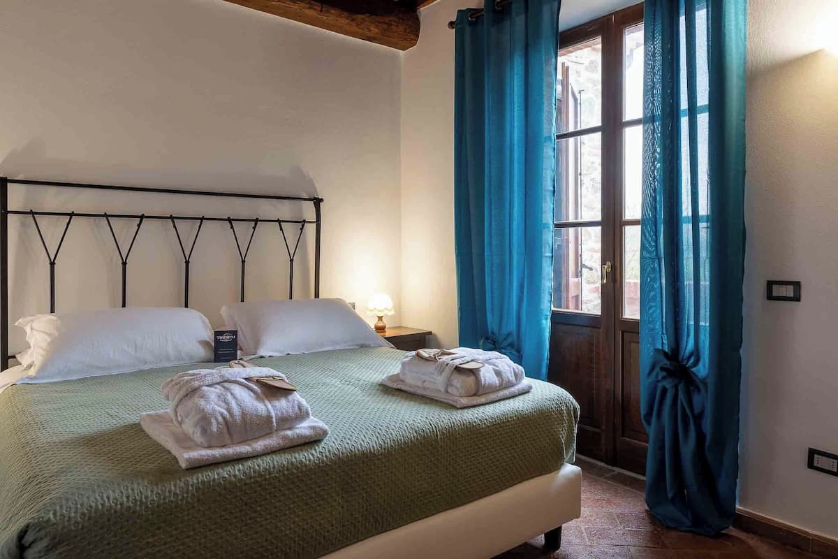 Een hotelkamer met een bed, nachtkastje, lamp en een raam met gordijnen.
