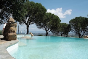 A clear swimming pool with a stone edge, surrounded by trees and a view of distant mountains. - Villa Tiberini Wine Relais (Torrita di Siena)