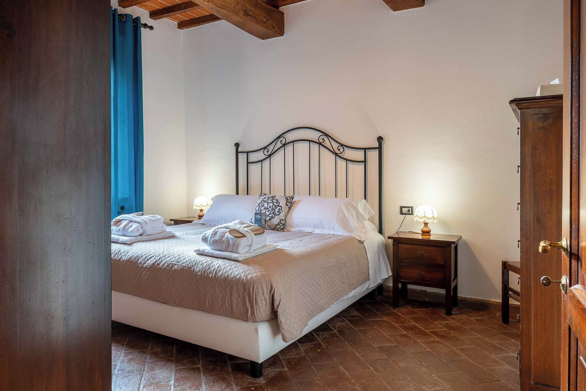 A neatly made bed with a headboard, a bedside table with a lamp, and a wardrobe in a room with tiled flooring.