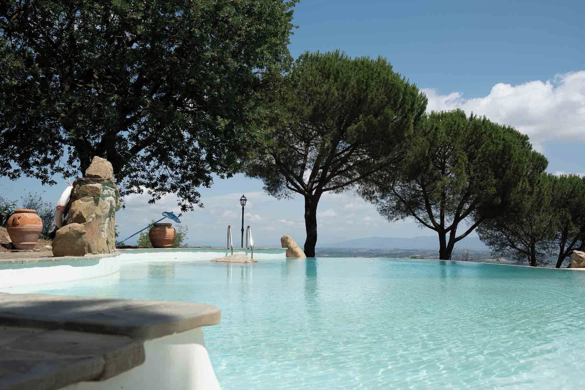 Une piscine à débordement à l’eau cristalline, entourée d’arbres et de rochers.