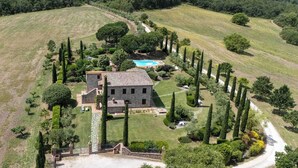 A stone building with a swimming pool, surrounded by well-manicured gardens and tall trees. - Villa Tiberini Wine Relais (Torrita di Siena)