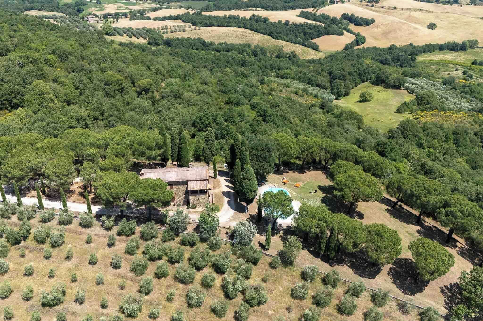 Una vista aerea di una proprietà con una grande casa circondata da alberi fitti, una piscina e un paesaggio collinare.