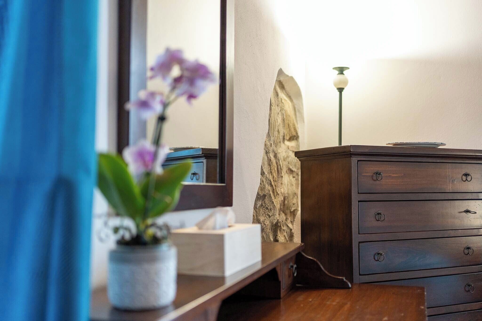 A wooden dresser with multiple drawers, a potted orchid, a stone accent wall, and a lamp.