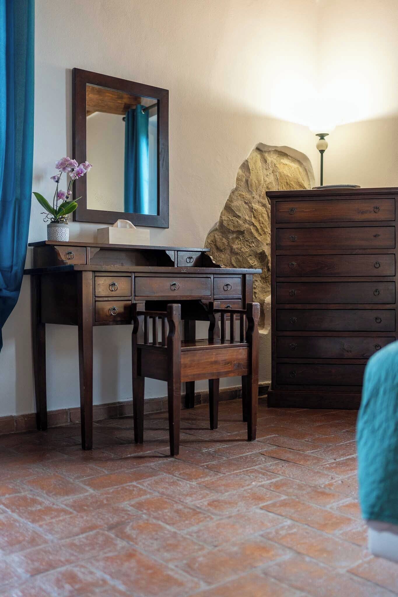 A wooden desk with drawers, a chair, a mirror, a potted plant, a dresser, and a lamp.