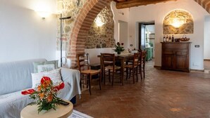 A cozy living room with a stone archway, a dining area with wooden chairs, and a kitchen with a stone wall and wooden cabinets. - Villa Tiberini Wine Relais (Torrita di Siena)
