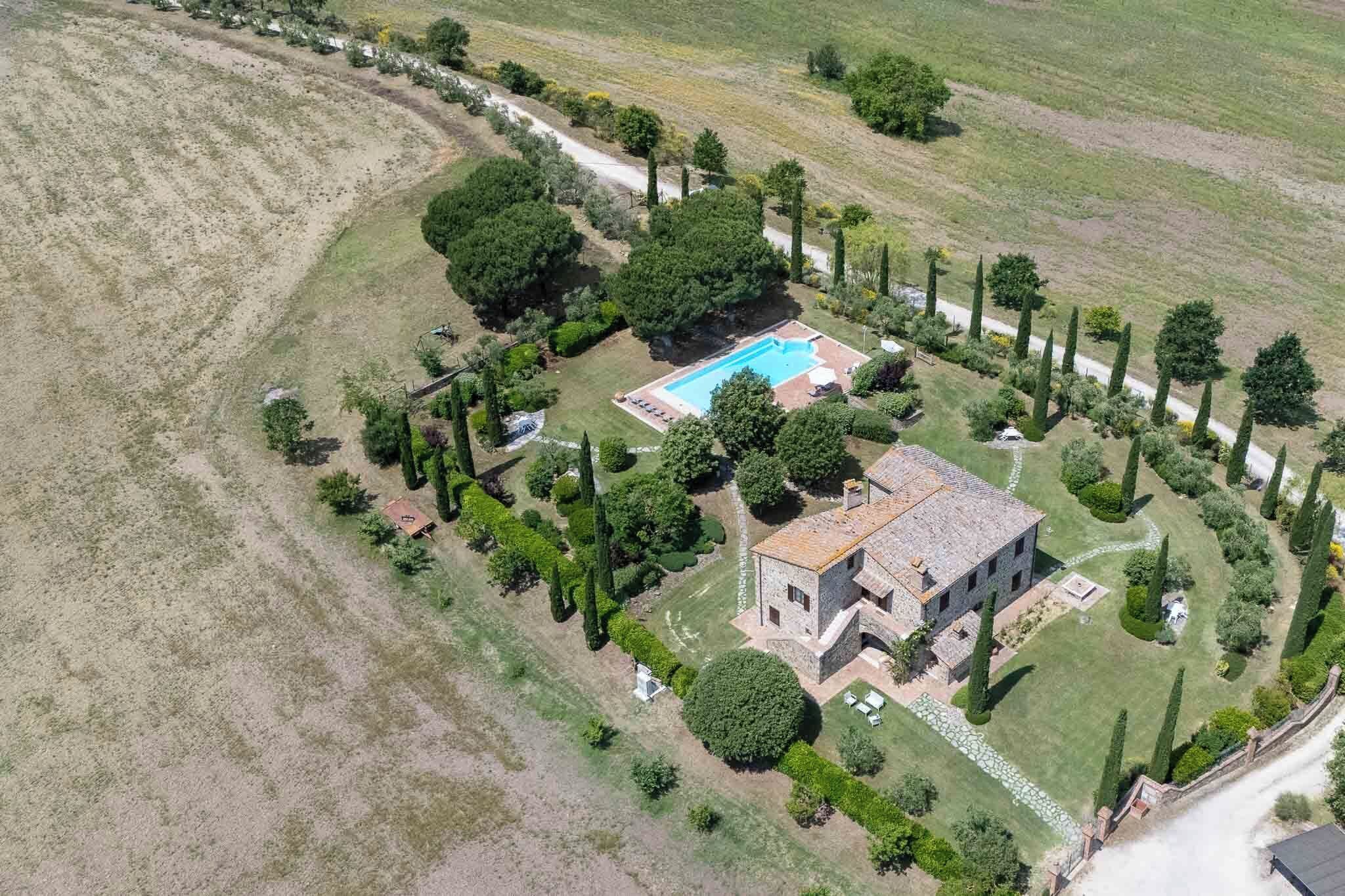 An aerial view of a property with a swimming pool, stone house, and landscaped garden.