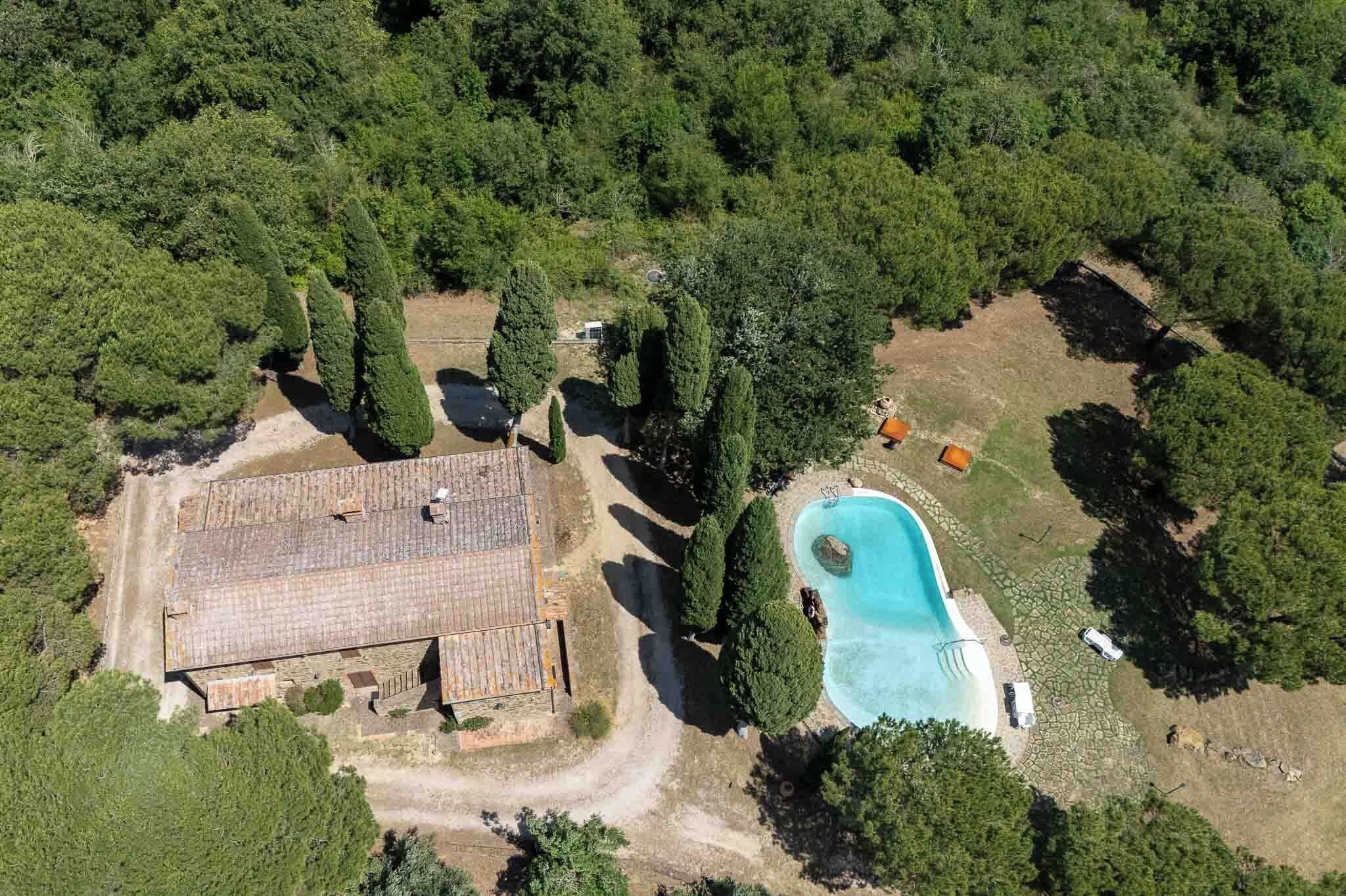 An aerial view of a property with a swimming pool, a large building, and surrounding greenery.
