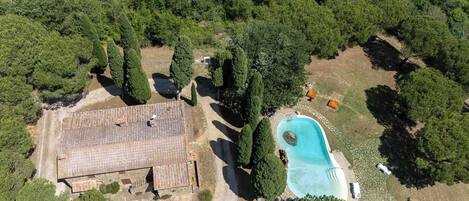 An aerial view of a property with a swimming pool, a large building, and surrounding greenery.