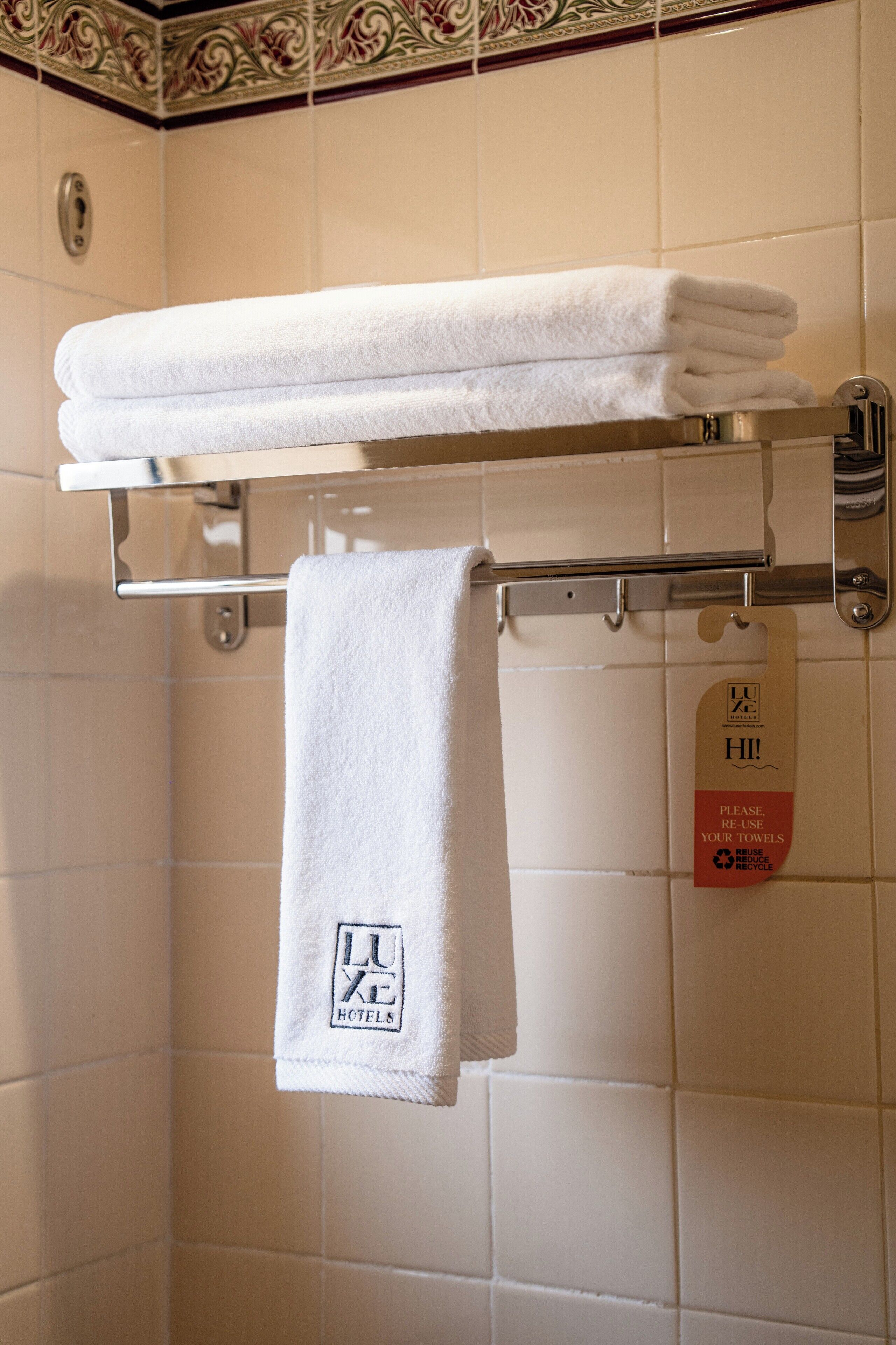 A bathroom with a towel rack holding folded towels and a tag instructing to reuse towels.