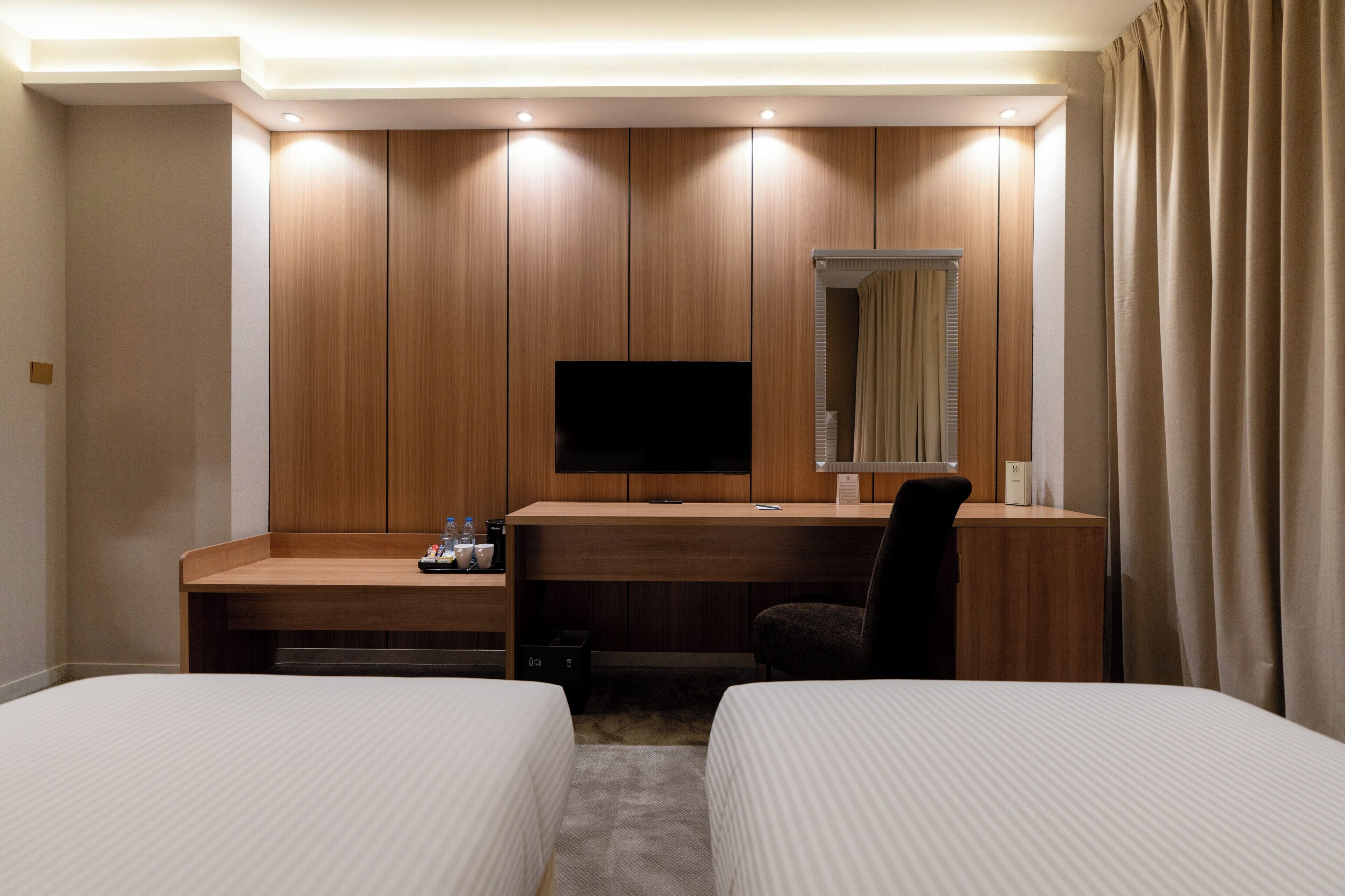 A hotel room with two beds, a desk with a TV, and a mirror.
