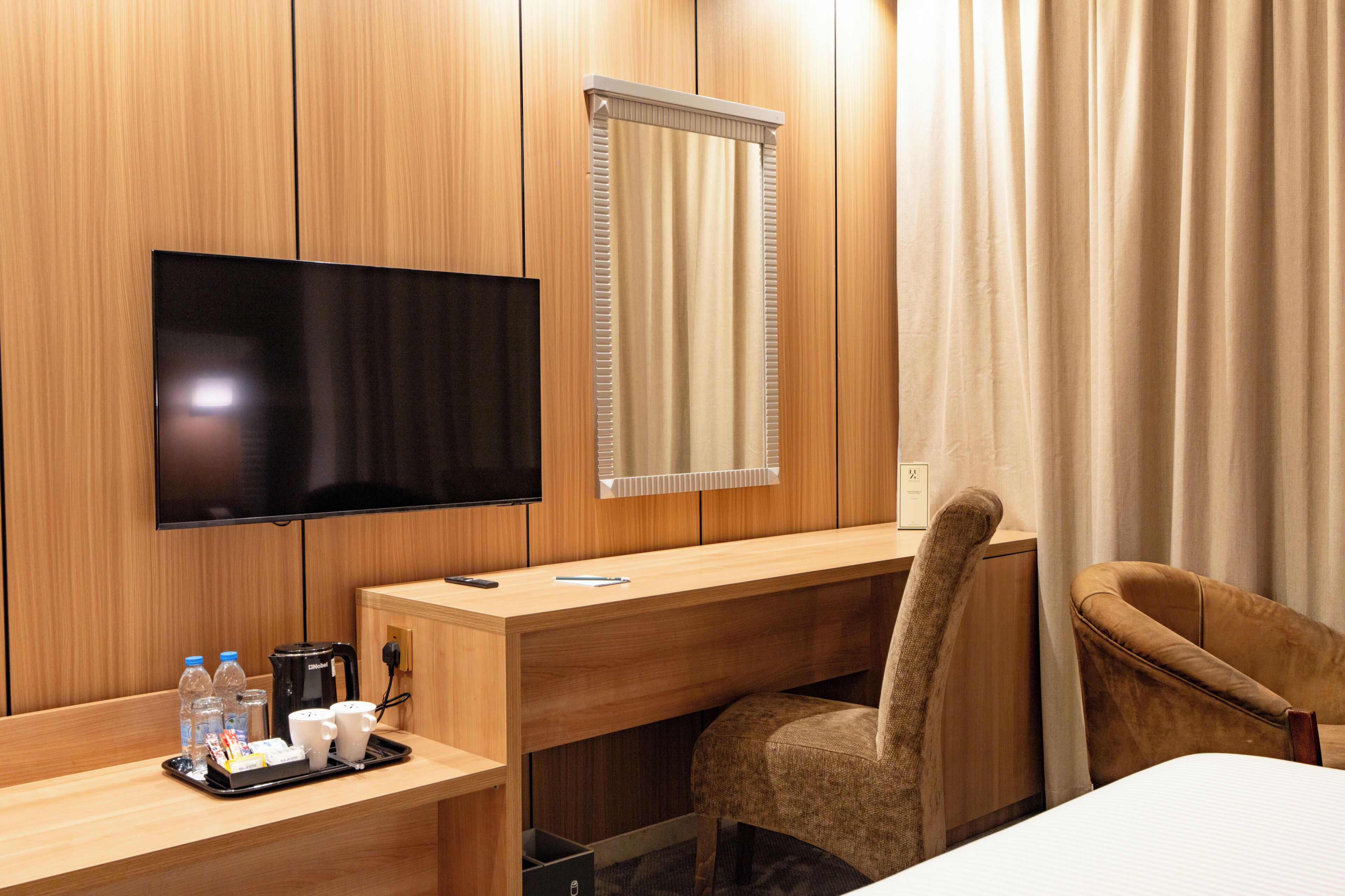 A hotel room with a wooden desk, a television, a chair, a bed, and a window with curtains.