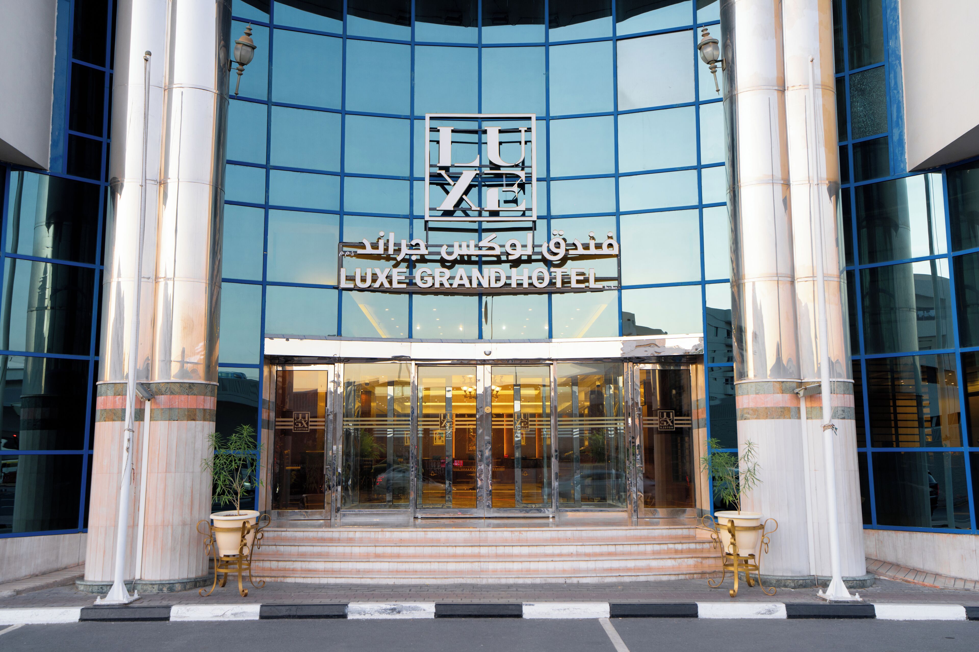 The entrance to the LUXE GRAND HOTEL with a glass facade and columns.