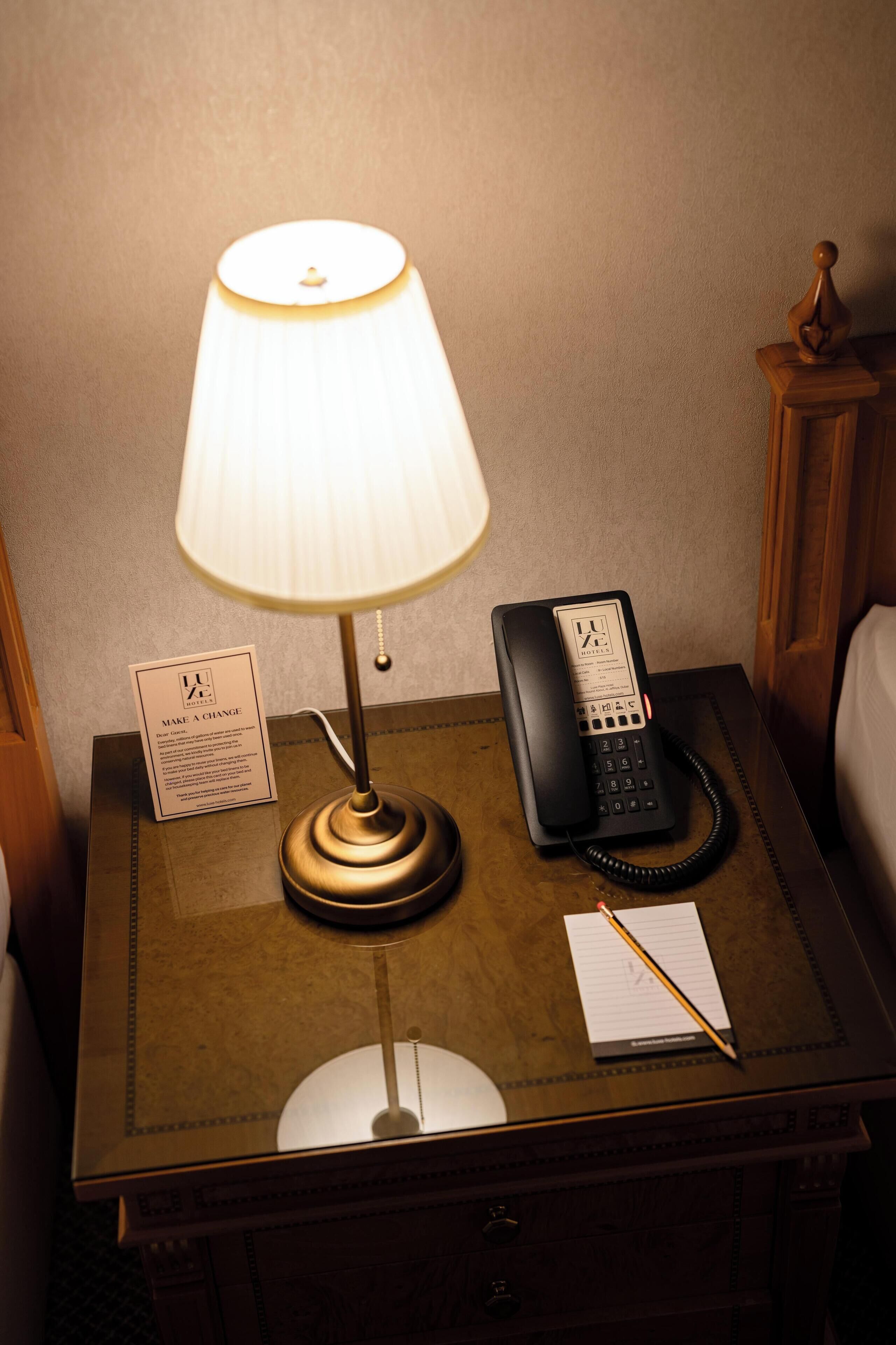 A wooden nightstand with a lamp, a telephone, a notepad, and a pen.