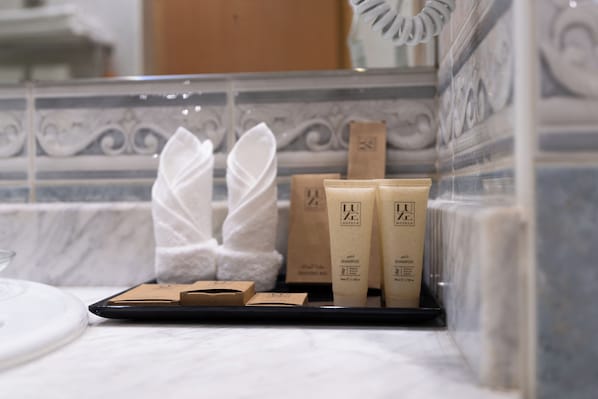 Des articles de toilette sont disposés sur un plateau dans une salle de bain dont un mur est recouvert de carreaux.